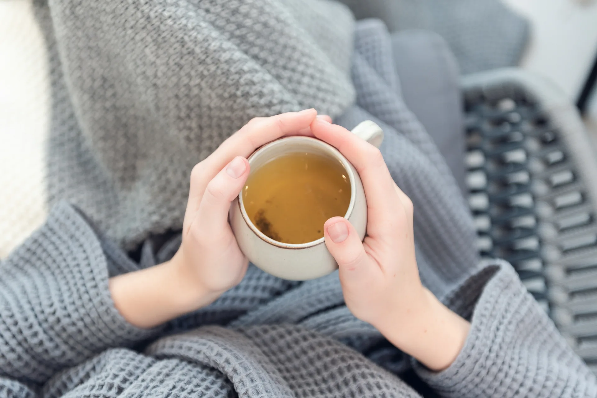 A cup of tea held in hands wrapped in a cosy blanket
